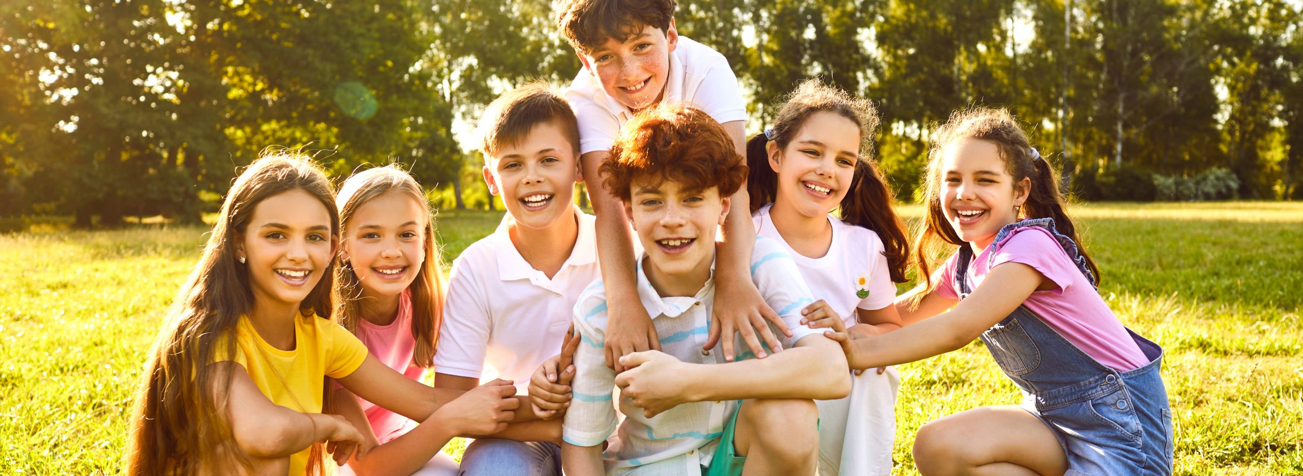 Happy children friends standing together outdoors, having fun and smiling in the park on holidays enjoying spending time in a summer camp. Portrait of a kids looking at camera. Banner.